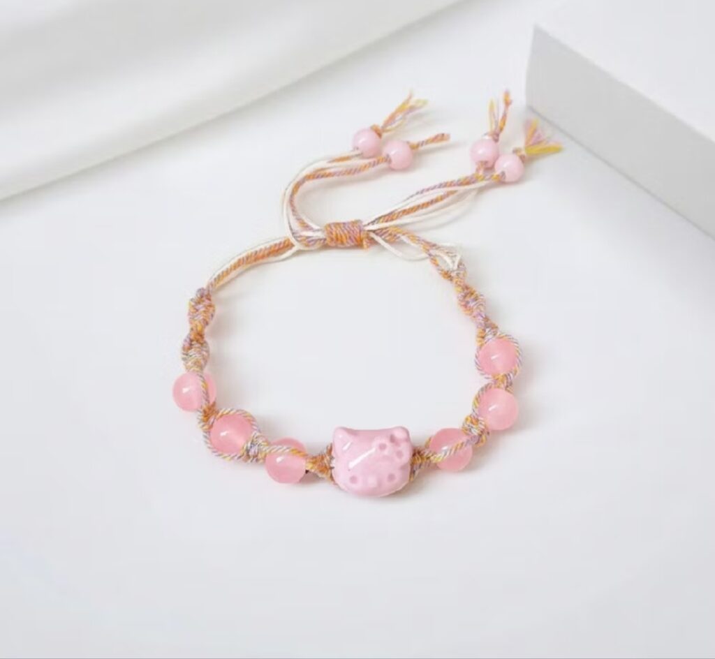 Gelang tali adjustable warna pastl dengan charm kepala kucing pink dan manik-manik pink mengkilap.